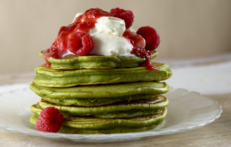 Green matcha pancakes topped with coconut cream, raspberries and raspberry coulis