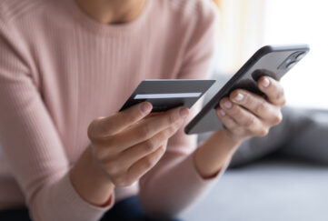 A women in a pink top close up of hands holding a credit card in one hand and phone in the other