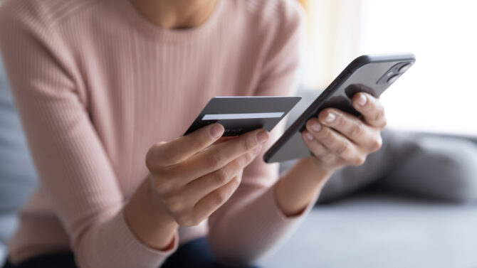 A women in a pink top close up of hands holding a credit card in one hand and phone in the other