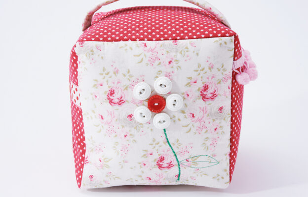 Close up of a patchwork doorstop with pink and white floral patch and red polkadot patch and a flower sewn on with buttons