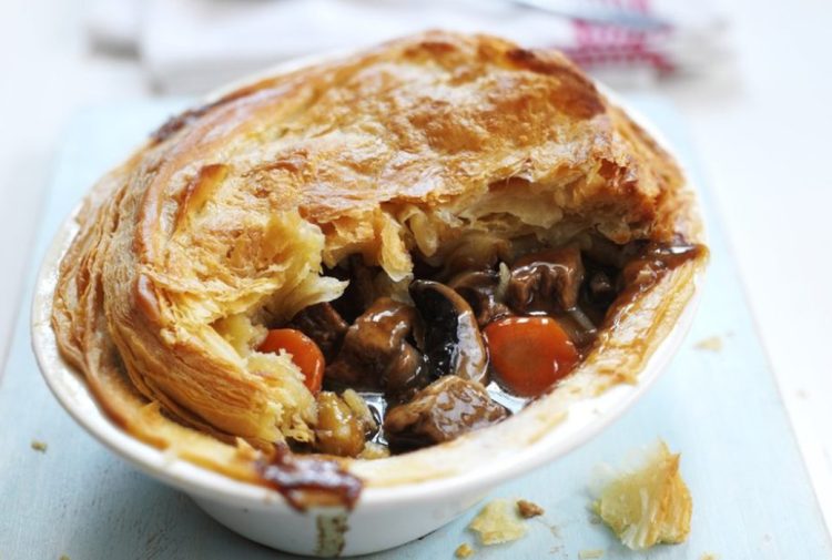 Quorn steak pie in a white dish, the filling visible through a hole in the pastry lid.