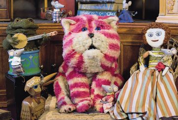 Best 70s Children's TV Programmes. Image shows bagpuss, the pink and white striped toy cat sat alongside his friends.