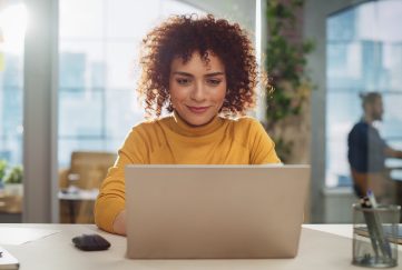 Young lady with curly short hair wearing yellow top, on her laptop