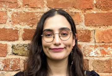 Smiling girl in her twenties with long brown hair and glasses.