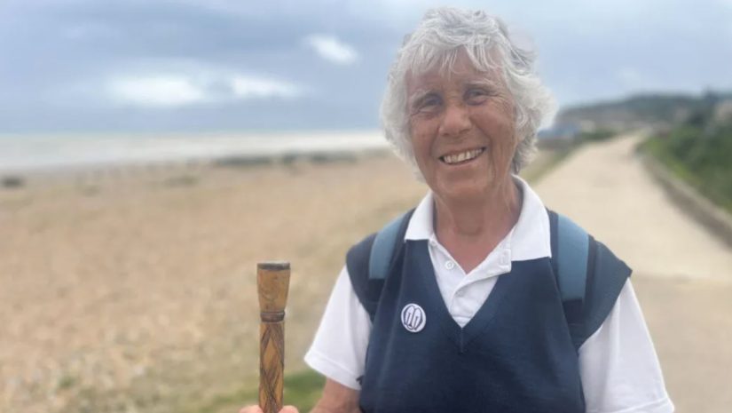 Successful people later in life. Pam Brooks who completed a 90-mile charity walk is seen standing on the beach front holding a walking pole having completed her trek. She is smiling wide.