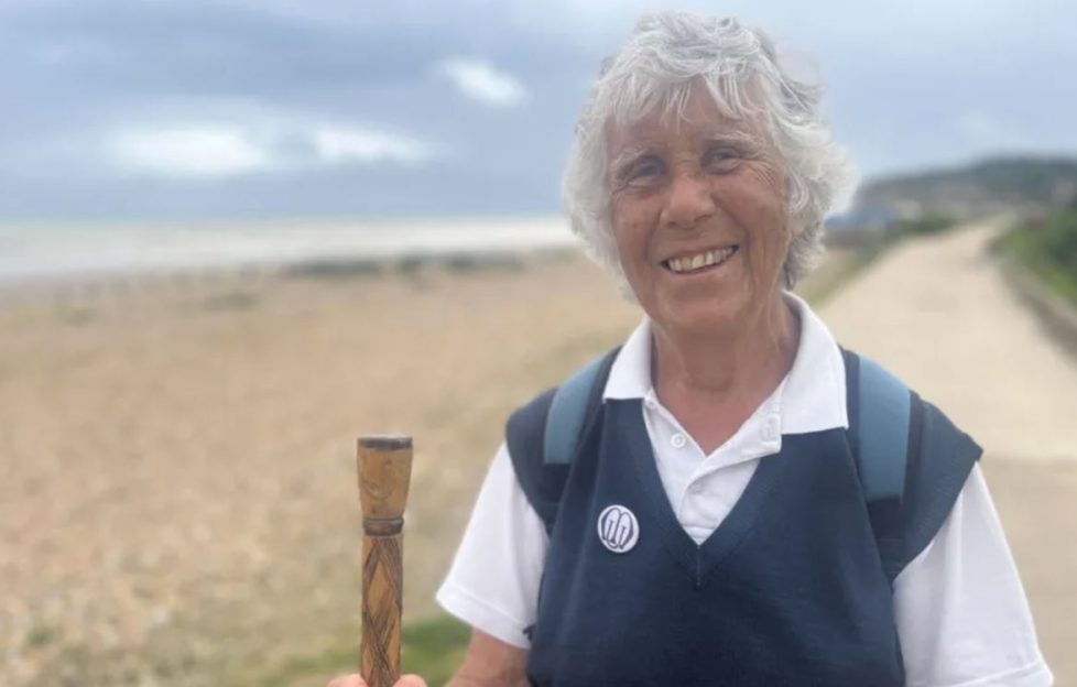 Successful people later in life. Pam Brooks who completed a 90-mile charity walk is seen standing on the beach front holding a walking pole having completed her trek. She is smiling wide.