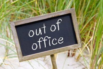 Chalkboard with the words 'Out Of Office' against backdrop of sand dunes.