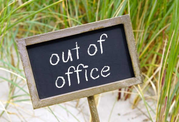 Chalkboard with the words 'Out Of Office' against backdrop of sand dunes.