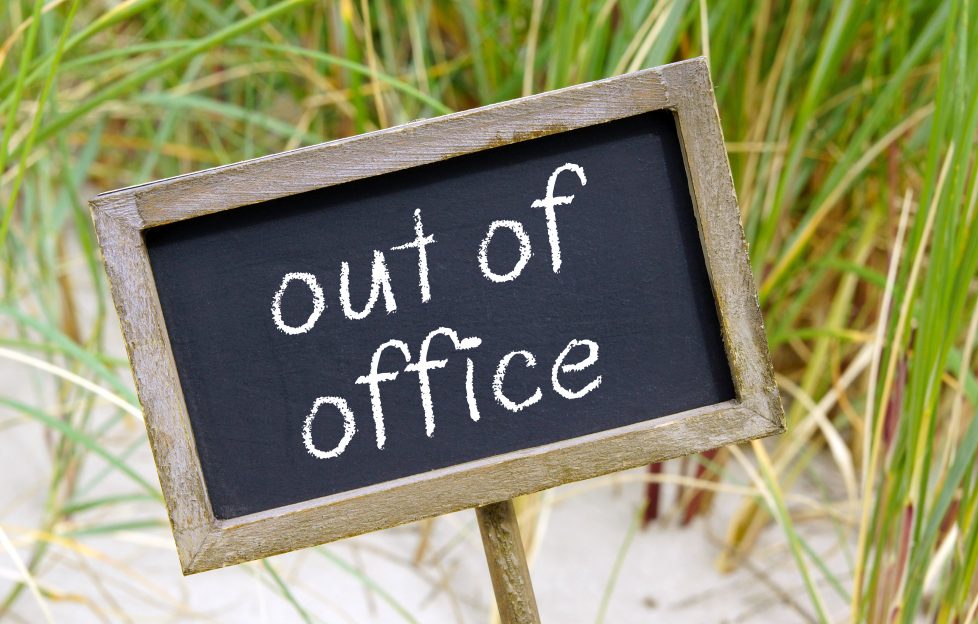 Chalkboard with the words 'Out Of Office' against backdrop of sand dunes.