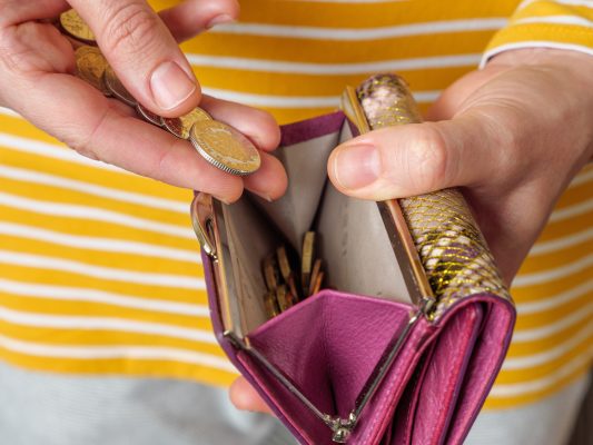 Women holding a pink purse and counting British coins into it.