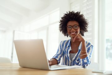 Smiley black lady wearing glasses and striped blouse, working on laptop.