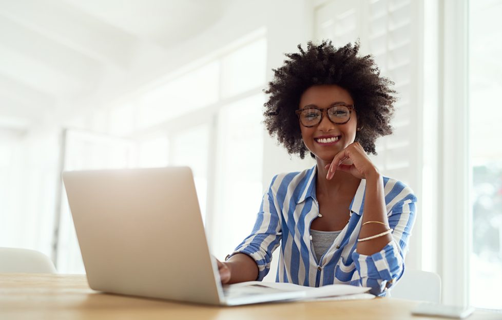 Smiley black lady wearing glasses and striped blouse, working on laptop.