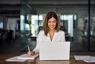 Brunette middle-aged lady with laptop, pen and notebook.