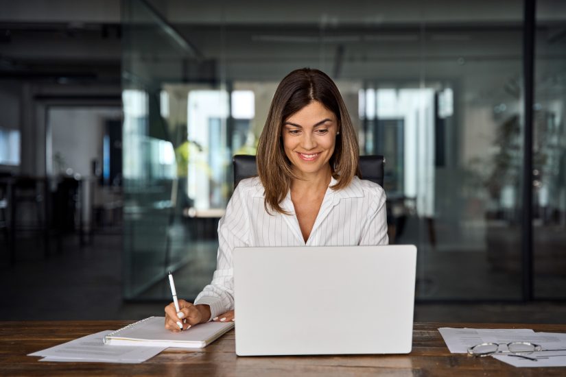 Brunette middle-aged lady with laptop, pen and notebook.