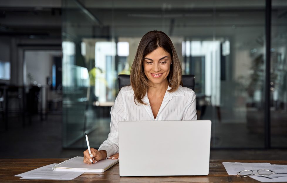 Brunette middle-aged lady with laptop, pen and notebook.