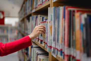 public libraries funding crisis. woman reaches into a library book shelf to pick a book.