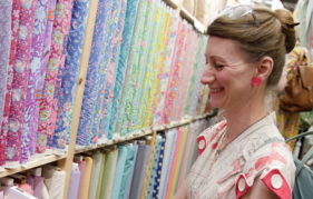 woman at one of the listed craft fairs, Festival of Quilts, looking at a colourful, quilt fabrics.