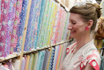 woman at one of the listed craft fairs, Festival of Quilts, looking at a colourful, quilt fabrics.