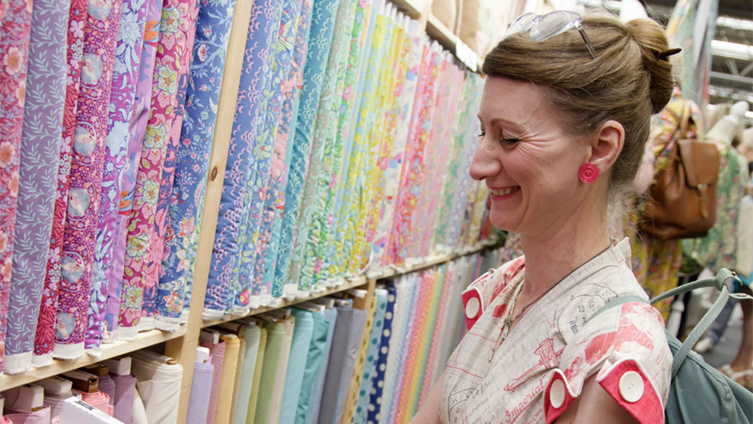 woman at one of the listed craft fairs, Festival of Quilts, looking at a colourful, quilt fabrics.