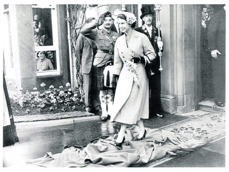 The Queen steps over a student's gown during her visit to Queen's College in 1955.