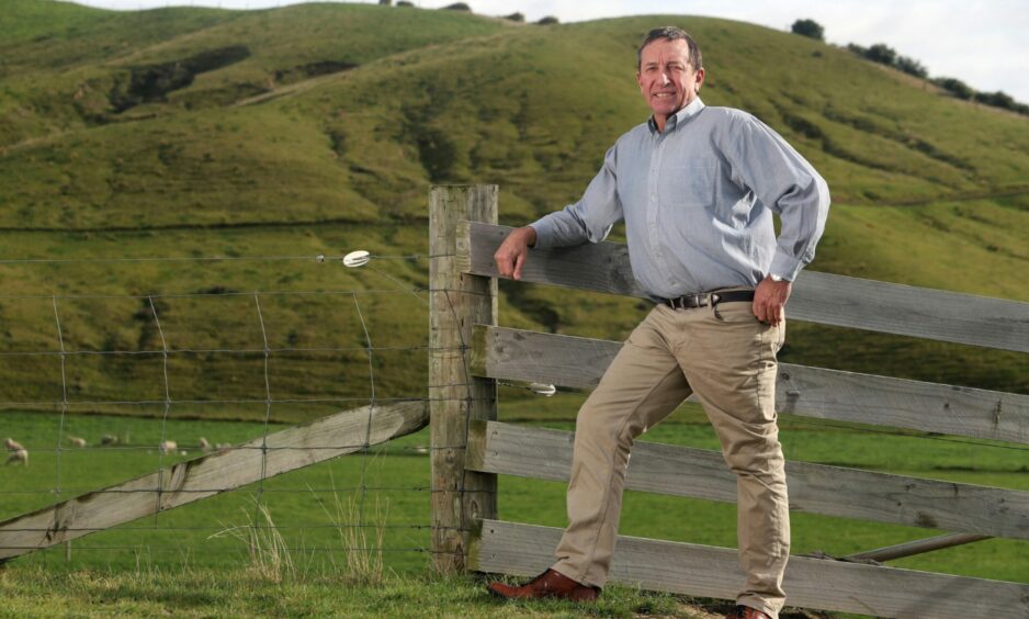 New Zealand farmer Doug Avery behind wellbeing programme stands at a fence in a green field.