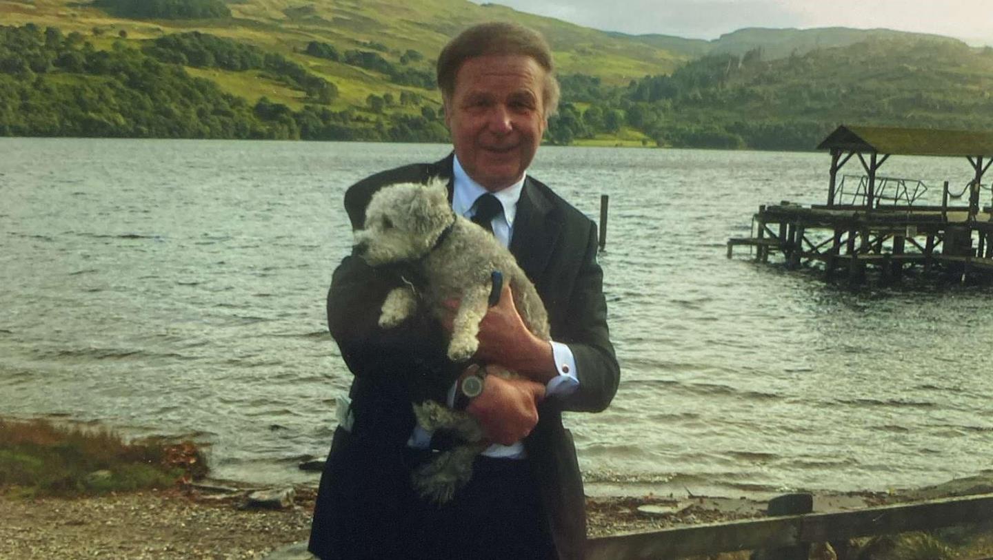 Dr Arnie Hornsby pictured by the water holding a dog.