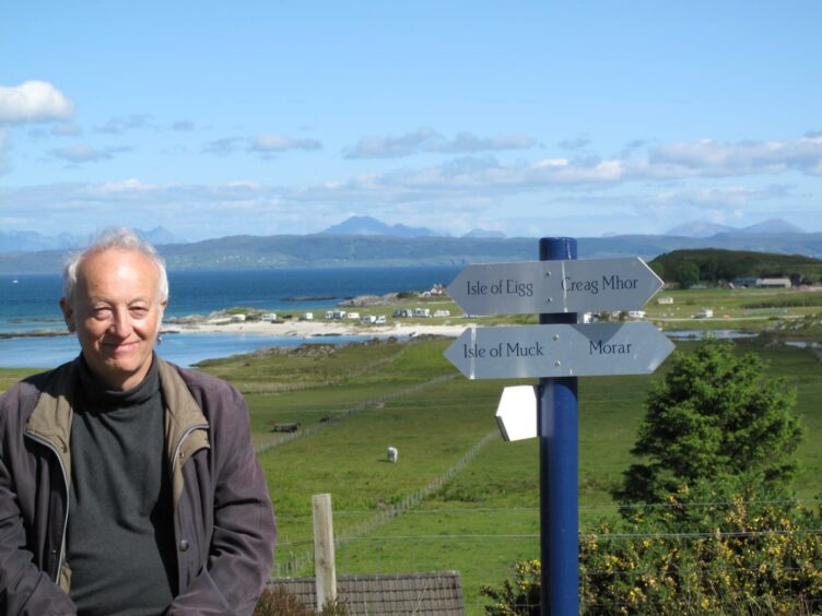 John, standing in front of a sign pointing to different highland locations. 