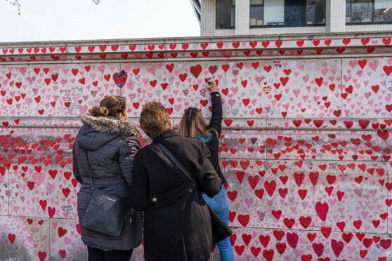 People add to the painted hearts at the national Covid memorial wall to remember the victims of the coronavirus pandemic. Amer Ghazzal/Shutterstock.