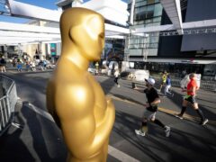 Runners move past Oscars statues already in place for the 2022 Academy Awards along Hollywood Blvd., during the 2022 Los Angeles Marathon Sunday, March 20, 2022 in Los Angeles. (David Crane/The Orange County Register via AP)