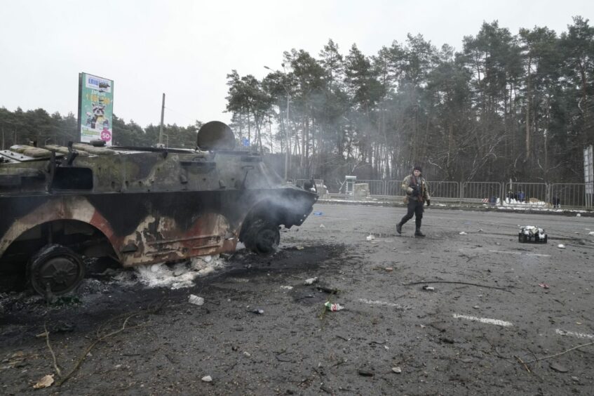 A volunteer of Ukraine's Territorial Defense Forces walks by a damaged armored vehicle at a checkpoint in Brovary, outside Kyiv, Ukraine. Picture by AP.
