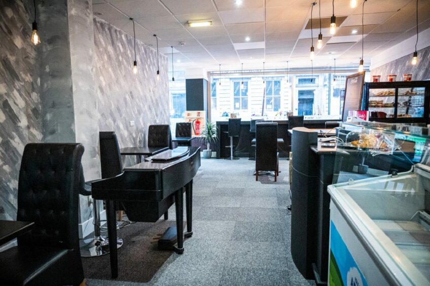 Inside Central Coffee Aberdeen's seating area, with tables and a piano to the right and a counter to the left, with more seating toward the front window