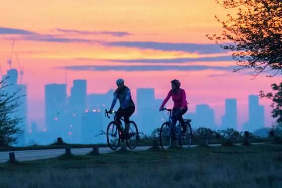 Cyclists make their way through Richmond Park in front of the London city skyline earlier this morning during sunrise. Easter weekend is set to be warm with temperatures expecting to reach 20C in London. Rick Findler/ Story Picture Agency.