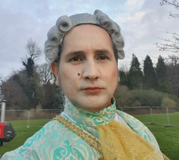 A selfie of Aaron in a regency-style grey wig and green, high-necked period clothes.