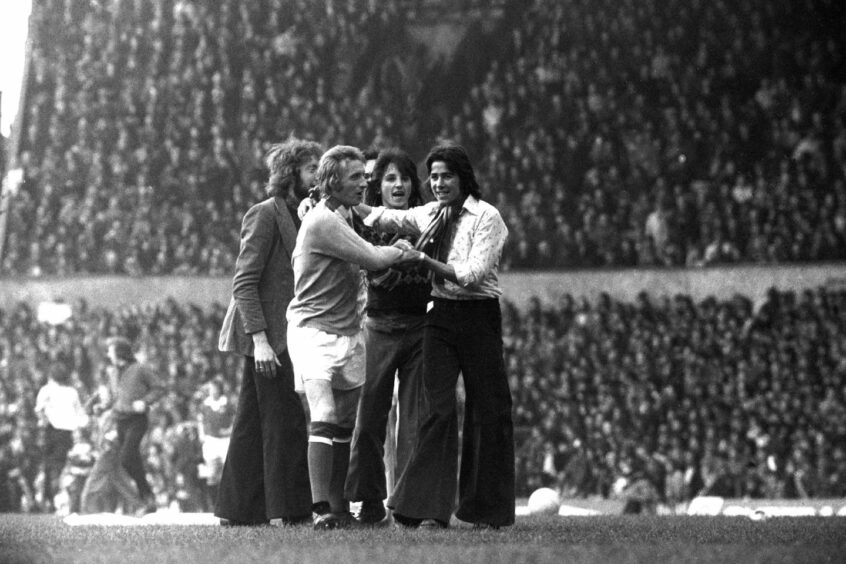 Manchester United fans wrap scarves around the neck of Manchester City's Denis Law following his 1974 goal.