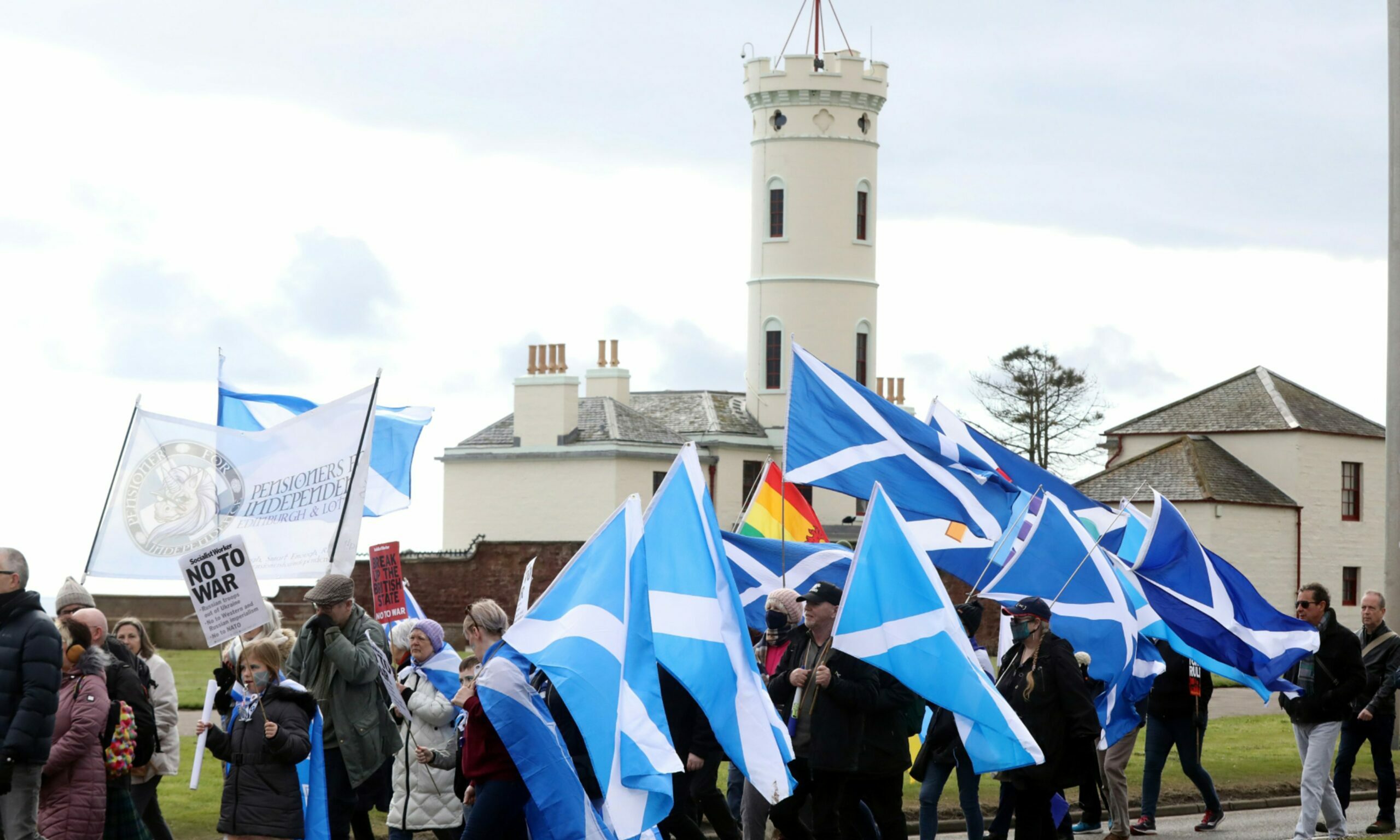 People holding up signs and waving Saltire flags in the air.