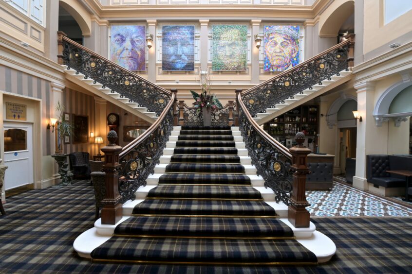 Double-sided staircase with white steps, wood and dark metal banisters and covered in tartan carpet.