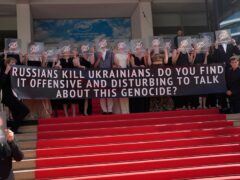 Filmmakers from the film ‘Butterfly Vision’ and festival goers participate in a demonstration by holding a banner that reads “Russians kill Ukrainians. Do you find it offensive or disturbing to talk about this genocide?” The participants cover their faces with transparent squares depicting the crossed eye as seen in social media when content is deemed sensitive or disturbing. The demonstration took place at the 75th international film festival, Cannes, southern France, Wednesday, May 25, 2022 (AP Photo/Petros Giannakouris)