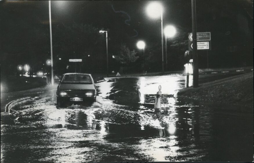 A car gets stuck in the water while negotiating the Old Glamis Road circle at Kingsway in 1977.