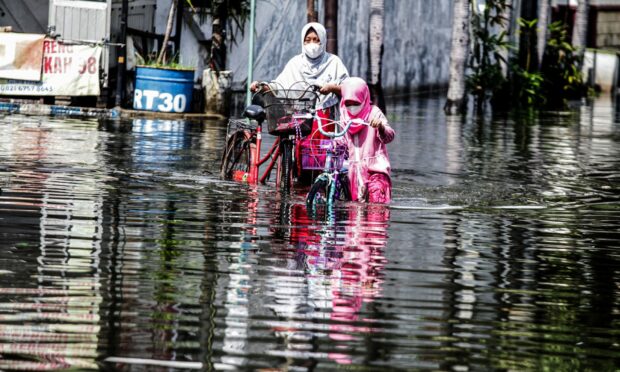 A mother and her daughter push their bikes through flood water after heavy rain at Waru in Sidoarjo, East Java, Indonesia.