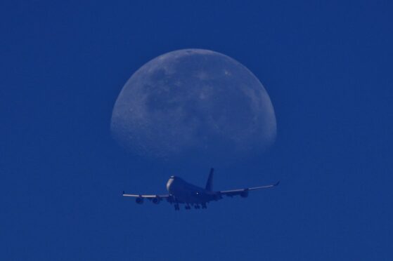 A commercial airplane descends towards Changi International Airport as the moon sets in Singapore. Suhaimi Abdullah/NurPhoto/Shutterstock.