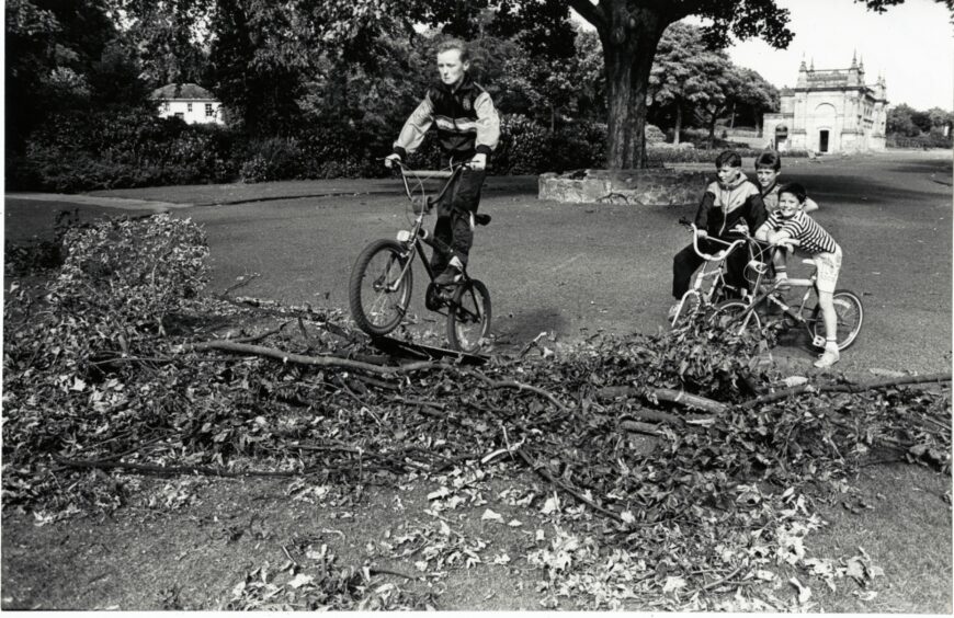 Spectators watch Andrew Fyffe go over the ramp of broken branches they made for their BMX bikes in Baxter Park.