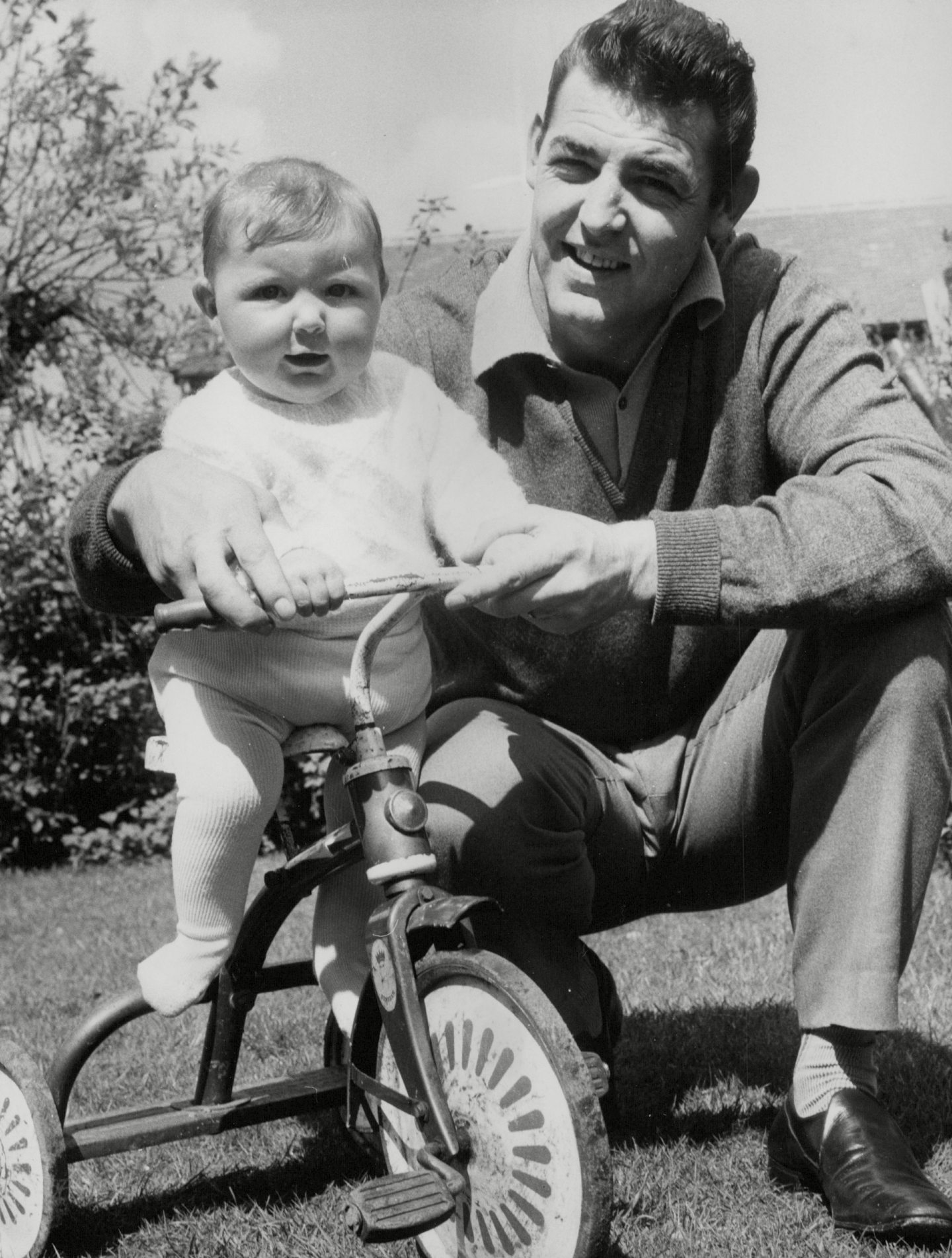 Adam Blacklaw kneeling next to his daughter Jane who is sitting on a tricycle