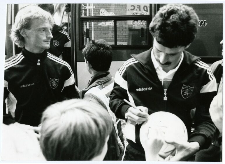 John Holt signs a ball for a young fan while Dave Bowman looks on after arriving home from Germany in 1987.