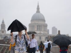 Pedestrians shelter under umbrellas as they cross the Millennium Bridge (Dominic Lipinski/PA)