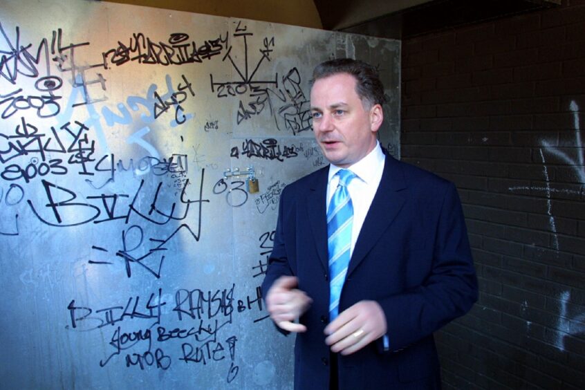 First Minister Jack McConnell standing beside a graffiti-covered wall in the down-at-heel complex.
