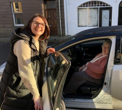 A woman holding a car door open for an elderly woman