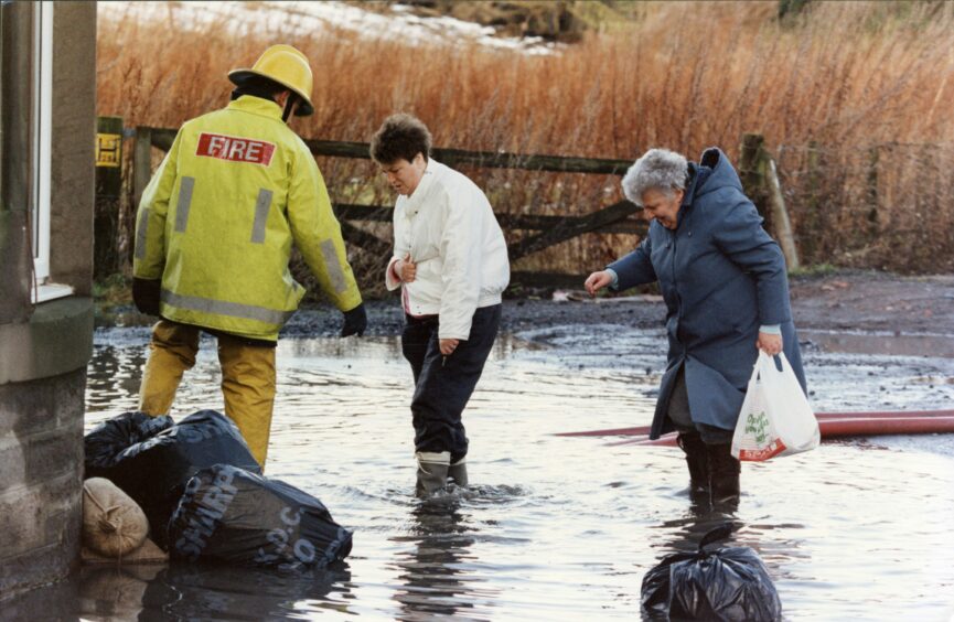 A fireman watches as two woman walk through a flooded area during the rescue operation. Image: DC Thomson.