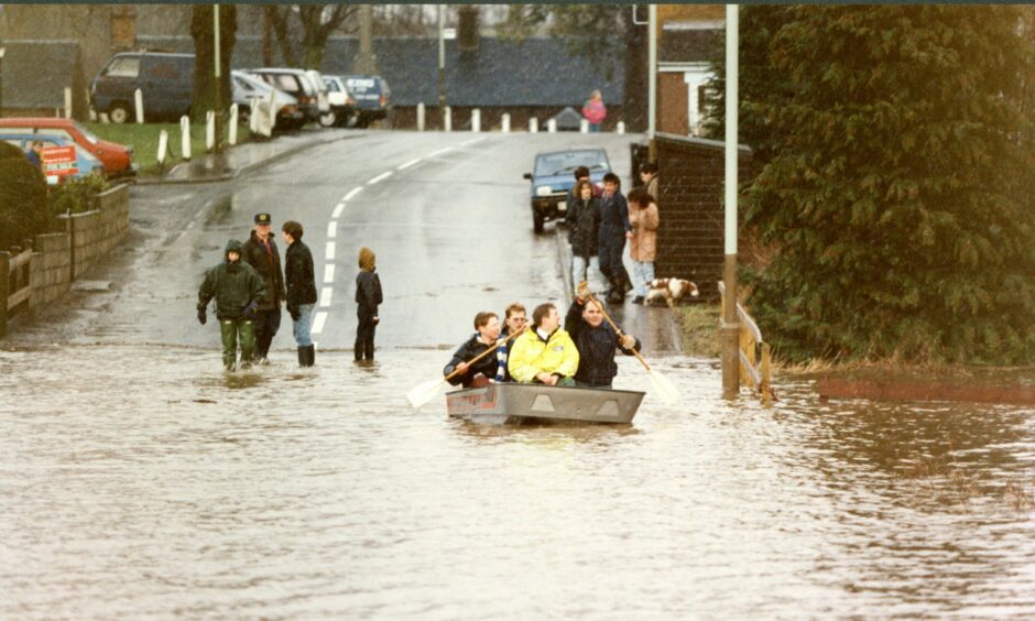People rowing a small boat across a flooded road at Spittalfield in Perthshire. Image: DC Thomson.