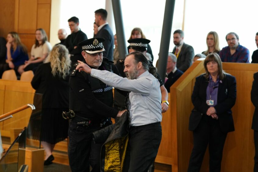 Police and security officers remove a protester from the chamber during First Minster's Questions.