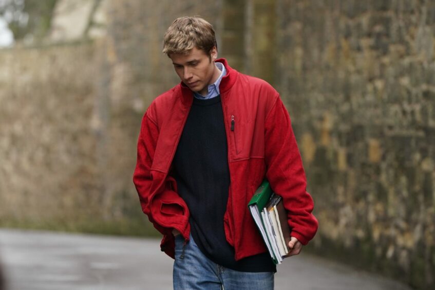 Actor Ed McVey, who plays Prince William, walking through a street in St Andrews with books in his hand during the filming of season six of The Crown.